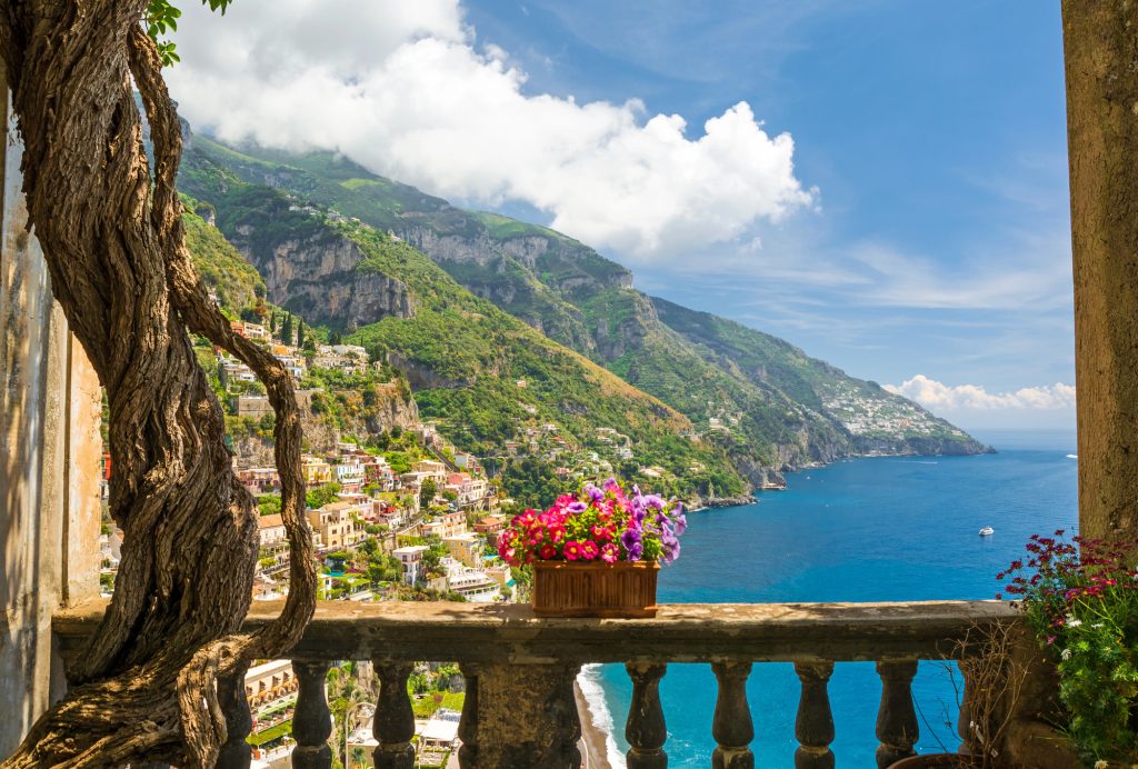 Scenic view of the Amalfi Coast from a balcony with turquoise sea, colorful cliffside villages, and lush hillsides.