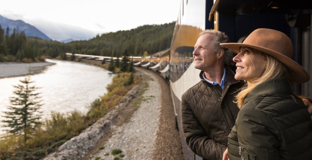 Couple on the viewing platform of a Rocky Mountaineer train enjoying sweeping views of the Colorado Rockies.